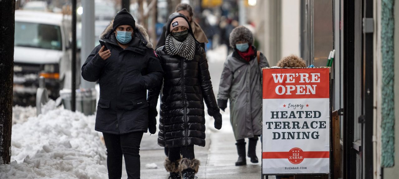 People walk past a "we're open, heated terrace dining" sign at Eli's Essentials on the Upper East Side on February 02, 2021 in New York City. (Photo by Alexi Rosenfeld/Getty Images)