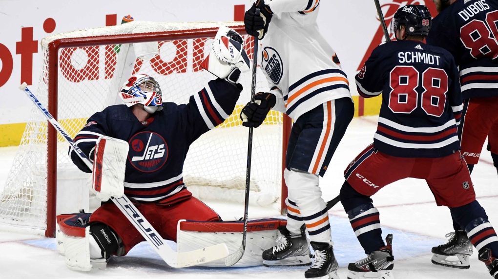 Winnipeg Jets goaltender Connor Hellebuyck (37) makes a a save as Edmonton Oilers' Jesse Puljujarvi (13) looks for the rebound during the second period of NHL action in Winnipeg, Tuesday, Nov. 16, 2021. THE CANADIAN PRESS/Fred Greenslade 