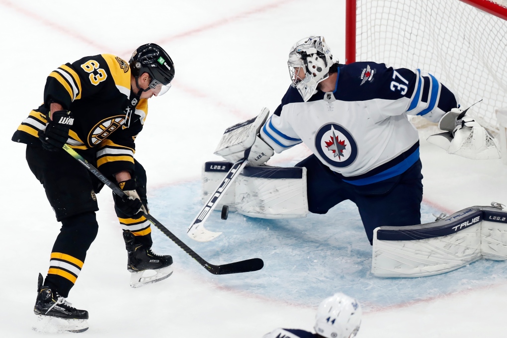 Winnipeg Jets' Connor Hellebuyck (37) blocks a shot by Boston Bruins' Brad Marchand (63) during the third period of an NHL hockey game, Saturday, Jan. 22, 2022, in Boston. (AP Photo/Michael Dwyer) 